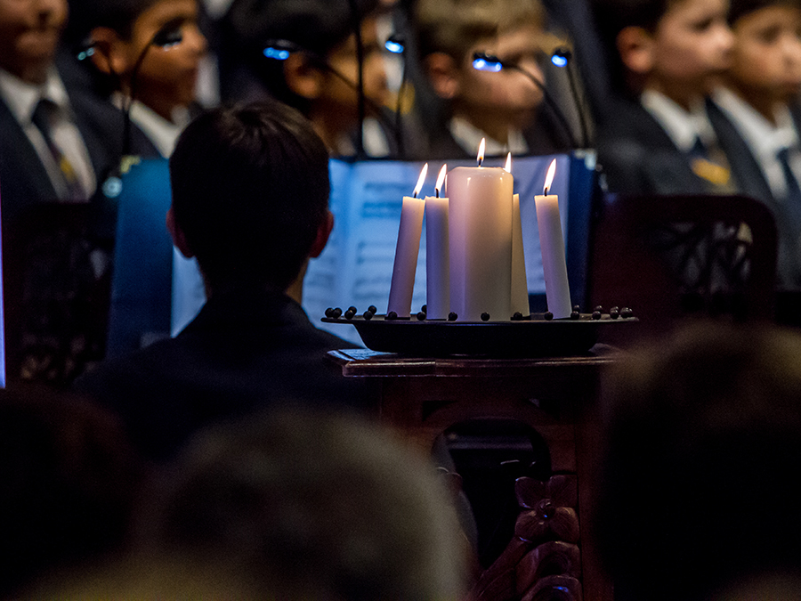 carols man playing piano with choir in background and candles in foreground